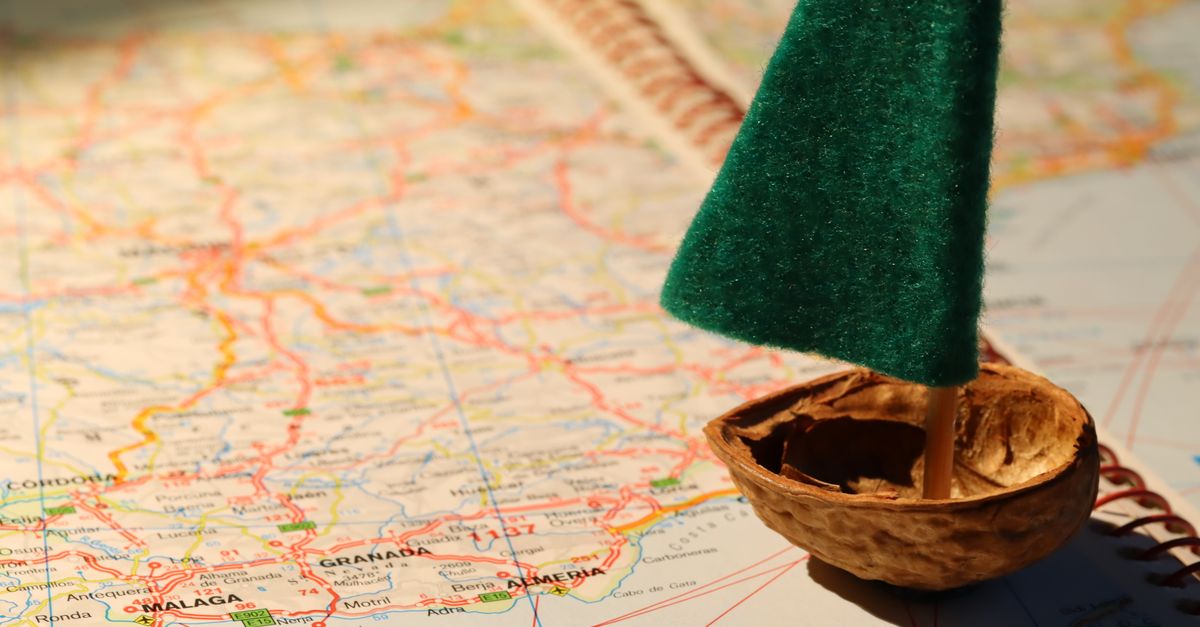 Creative travel metaphor with a tiny sailboat on a detailed world map.
